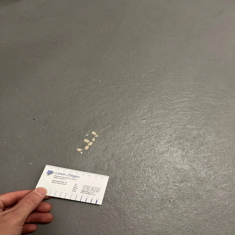 Abplatzungen Bodenbeschichtung in einem Kellerraum, meist aufgrund unzureichender Untergrundvorbereitung.